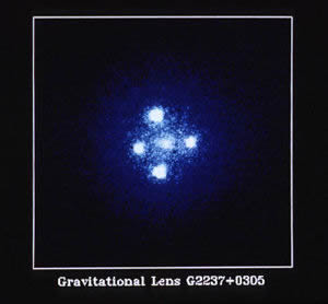 Fig. 1 - La Lente Gravitazionale G2237 + 0305 o Croce di Einstein. La galassia a spirale nel centro dell’immagine funge da lente gravitazionale mostrando attorno a sé quattro immagini dello stesso quasar a forma di croce. Il quasar è distante circa 9 milardi di anni-luce mentre la galassia dista 400 milioni di anni-luce. Crediti NASA, ESA e STScI. Vedi http://hubblesite.org/newscenter/archive/releases/1990/20/image/a/